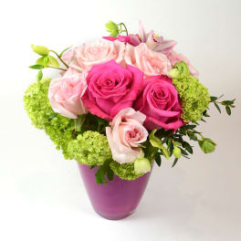 Pink and pale roses arranged in a purple vase with green hydrangea accents