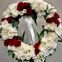 Circular wreath of red and white flowers on an easel with a white ribbon