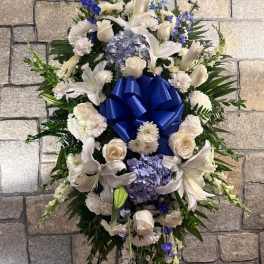 Standing floral spray with white lilies, roses, and blue flowers around a blue bow