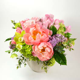 Pink and peach flowers arranged in a white vase with green accents