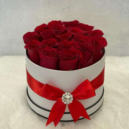 Round white hatbox of red roses with a red ribbon bow on a soft white surface