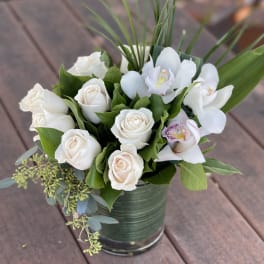 White roses and orchids arranged in a green tin container