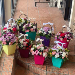 Bright mixed flower arrangements in colorful handled gift boxes with ribbon bows on outdoor steps