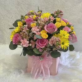 Pink and yellow mixed flower arrangement in a pink gift box with ribbon