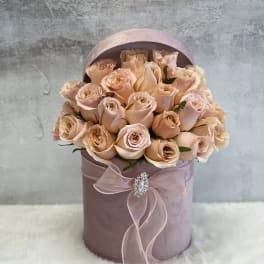 Round blush hatbox filled with peach roses and tied with a sheer pink bow