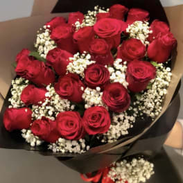 Hand-tied bouquet of red roses with white filler flowers wrapped in black and kraft paper