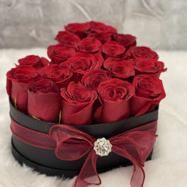 Heart-shaped black box filled with red roses and tied with a red bow and jewel accent