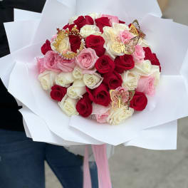 Large bouquet of red, white, and pink roses wrapped in white paper with gold butterflies and a crown