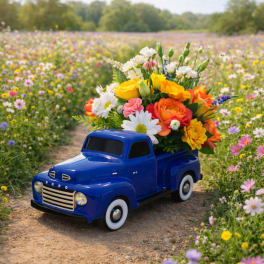 Blue ceramic toy truck filled with bright yellow, orange, white, and pink flowers on a path