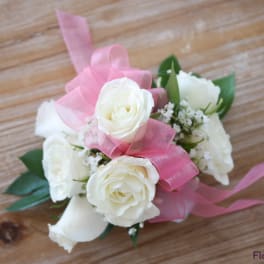 White rose corsage with pink ribbon on a wooden surface