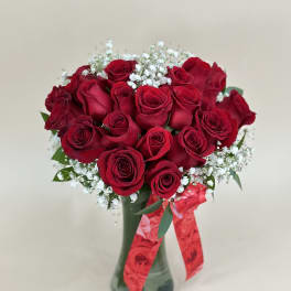 Arrangement of red roses with white filler flowers in a glass vase with a red ribbon