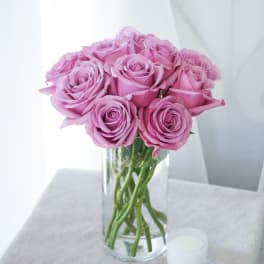 Pink roses arranged in a clear glass vase beside a small white candle