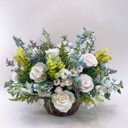Basket arrangement of white roses, blue flowers, and yellow blooms