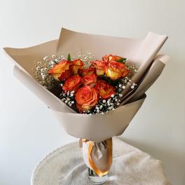 Bouquet of orange-red roses with baby's breath in tan wrapping