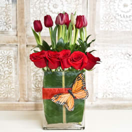 Red roses and tulips in a square glass vase with a butterfly decoration
