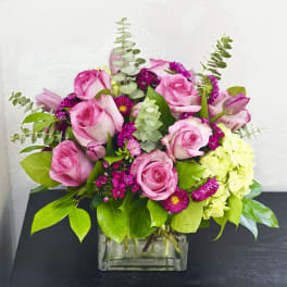 Pink roses and magenta flowers in a clear square vase