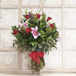 Bouquet of red roses and pink lilies in a glass vase with a red ribbon