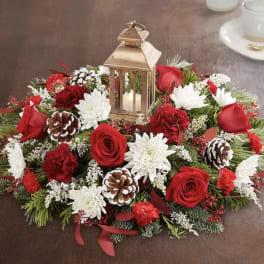 Round floral centerpiece with red roses, white mums, pinecones, and a lantern
