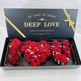 Black gift box of red roses arranged in clustered shapes with small white filler blooms.