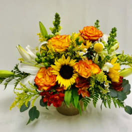 Bouquet of orange roses, sunflowers, and white lilies in a burlap-wrapped container