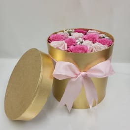 Round gold hatbox of pink and pale roses with lid and pink ribbon bow.