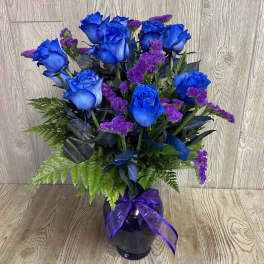 Blue roses and purple filler flowers in a dark vase with a ribbon