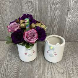 Pink and purple flower arrangement in a unicorn mug beside an empty matching mug