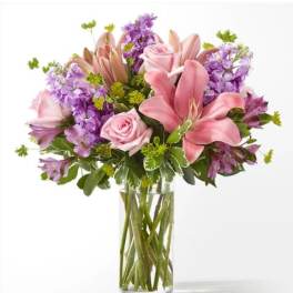Pink lilies and roses in a clear glass vase with purple flowers
