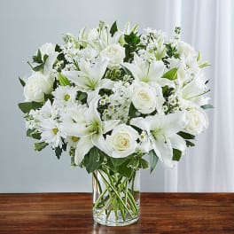 White lilies, roses, and daisies arranged in a clear glass vase