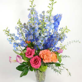 Tall bouquet of blue flowers with pink and peach roses in a clear vase