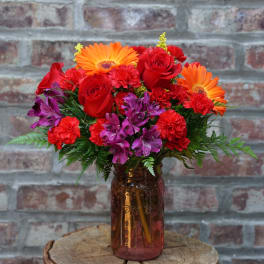 Bouquet of red roses, orange gerbera daisies, and purple flowers in a glass vase