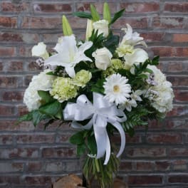 White floral arrangement with lilies, roses, and a ribbon bow