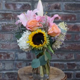 Bouquet of pink lilies, peach roses, and a sunflower in a glass vase