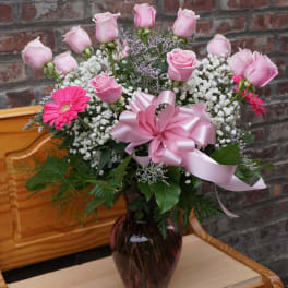 Pink roses and gerbera daisies in a vase with a pink ribbon