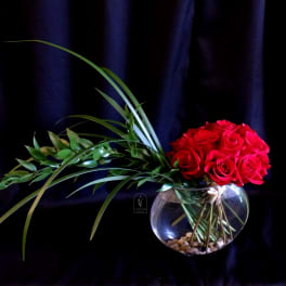 Red roses arranged in a round glass vase with long green leaves