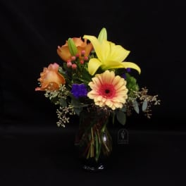 Mixed bouquet with yellow lily, peach roses, and a gerbera daisy in a glass vase