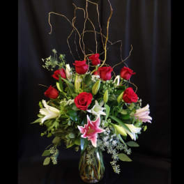 Red roses and white lilies in a glass vase with tall curly branches