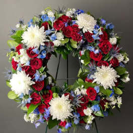Circular wreath of red roses, white chrysanthemums, and blue flowers on a stand