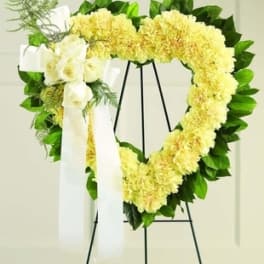 Heart-shaped yellow floral wreath on a stand with white ribbon
