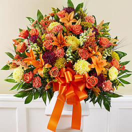 Large bouquet of orange and pink flowers with a ribbon in a white vase