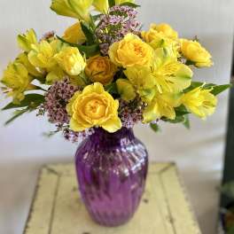 Yellow roses and alstroemeria in a purple glass vase