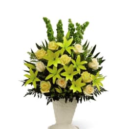Yellow roses and lilies arranged in a white pedestal vase