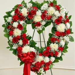 Heart-shaped wreath of red and white flowers on a stand with a red bow