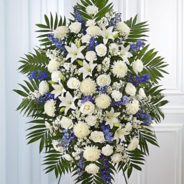 Standing funeral spray of white flowers with blue accents on a tripod easel