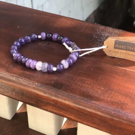 Purple beaded bracelet on a wooden shelf with a paper tag