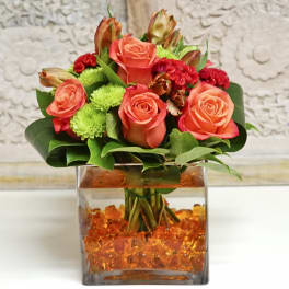 Coral roses and red flowers arranged in a square glass vase