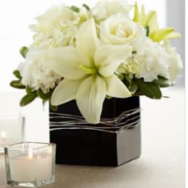 White lily and rose arrangement in a black square box with a candle nearby