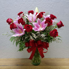Bouquet of red roses and pink lilies in a glass vase with a red ribbon