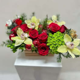 Red roses and pale yellow orchids in a low rectangular container