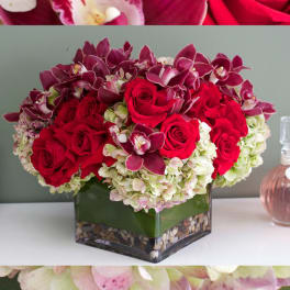 Red roses and purple orchids in a square glass vase
